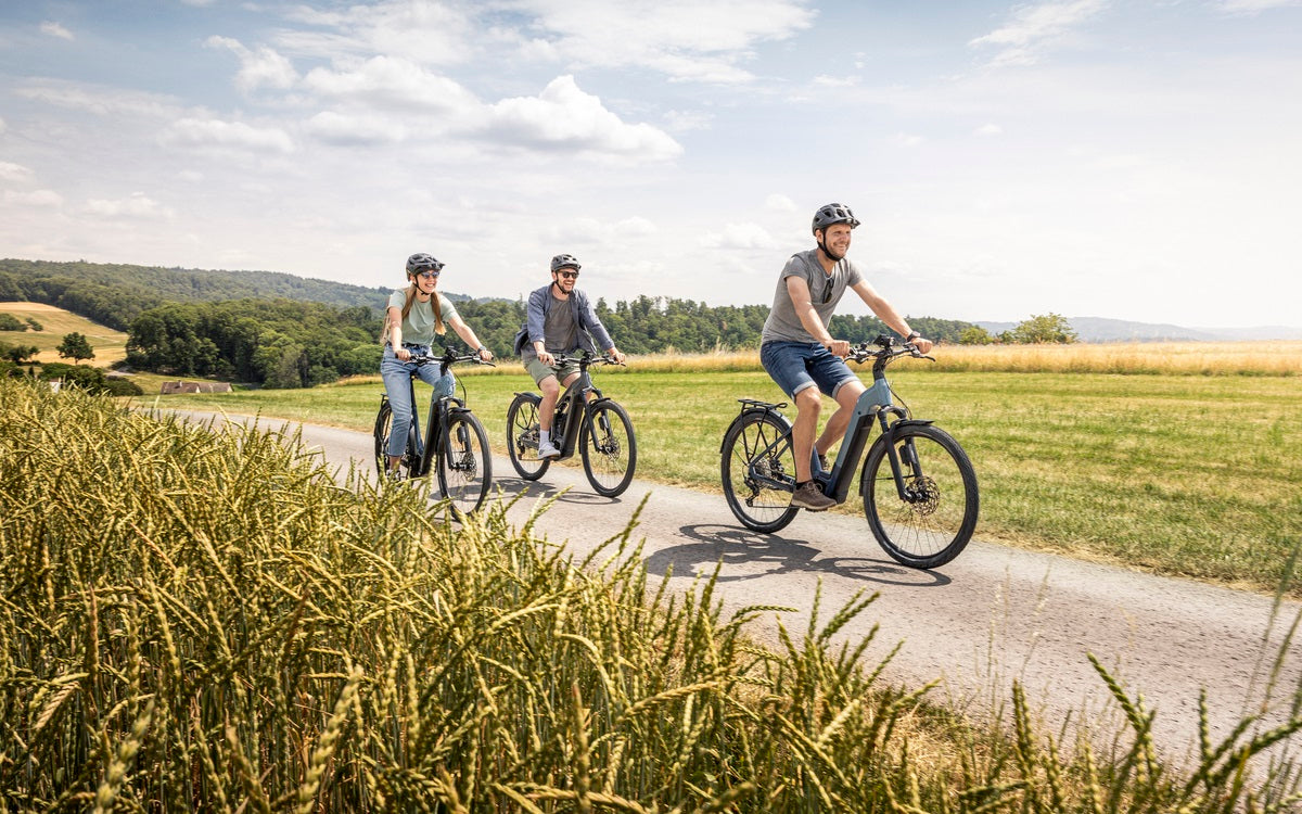 Drei Personen fahren auf E-Bikes der Marke Focus durch eine ländliche Landschaft, ideal für Freizeitfahrten.