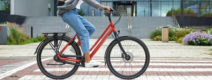 Rotes Gazelle mit Gepäckträger, dazwischen gehende Person. Einsatz für Stadtverkehr geeignet. Modernes Design.