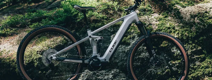 Silbernes Cube Stereo Hybrid One22 im Wald, geeignet für Offroad-Abenteuer, mit robusten Reifen und moderner Federung.