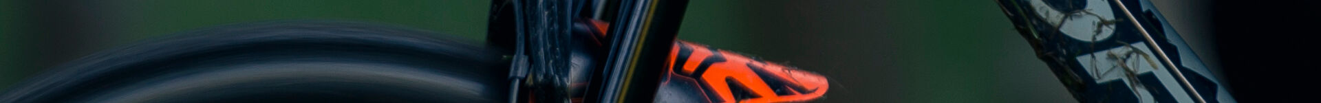 Teilansicht eines Fahrrads mit einem orangefarbenen Detail und unscharfem Hintergrund, möglicherweise ein Orbea Laufey Junior.