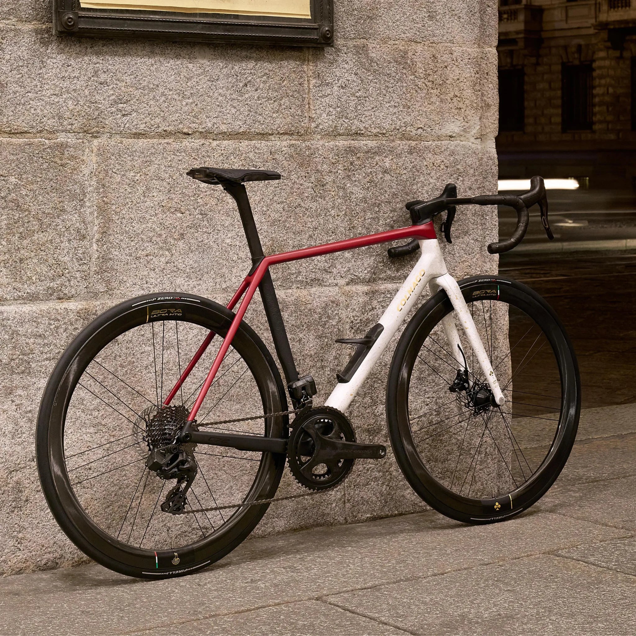 Colnago C72 Rennrad mit rot-weißem Rahmen und schwarzen Reifen, an Steinwand gelehnt. Für Straßenrennen und sportliche Radfahrer geeignet.