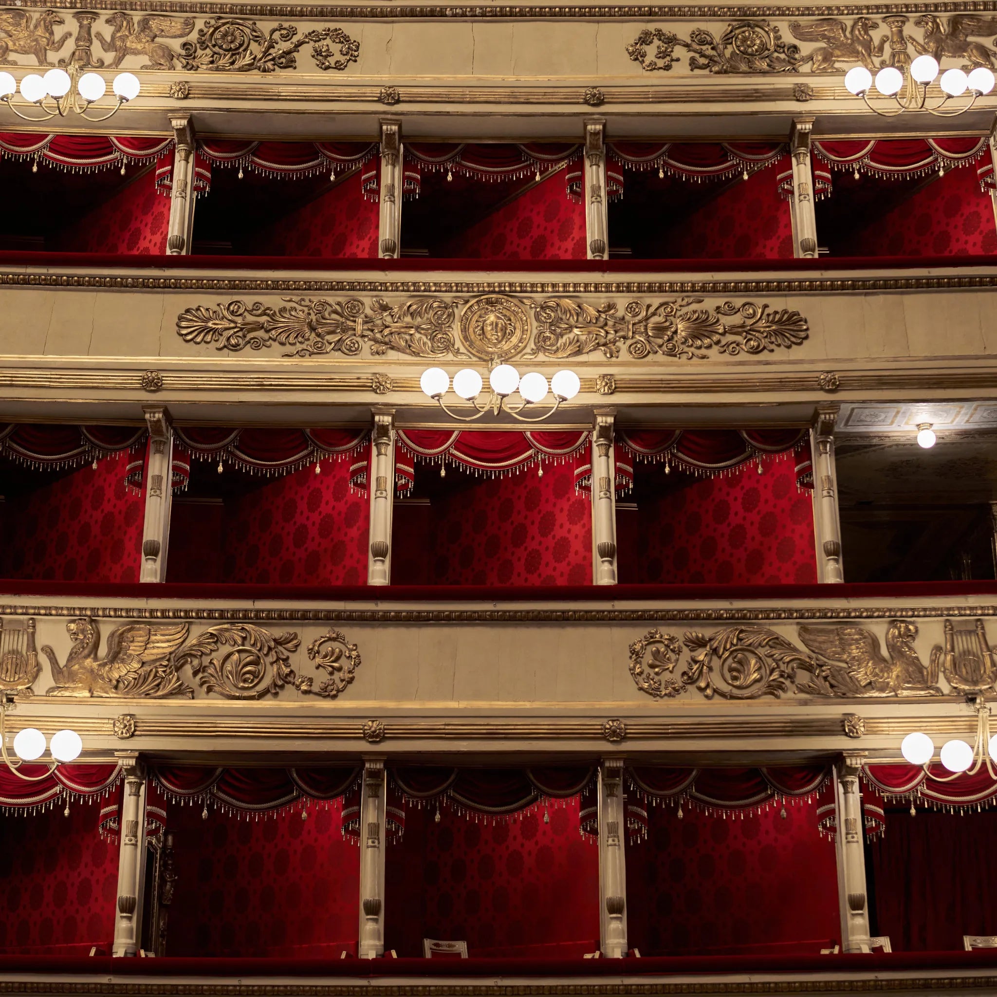 Rote Theaterlogen mit goldener Verzierung und Beleuchtung in einem klassischen Opernhaus.