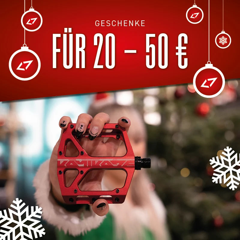 Rotes Fahrradpedal von Kacta, gehalten von Hand; Geschenke für 20-50 € im Hintergrund.