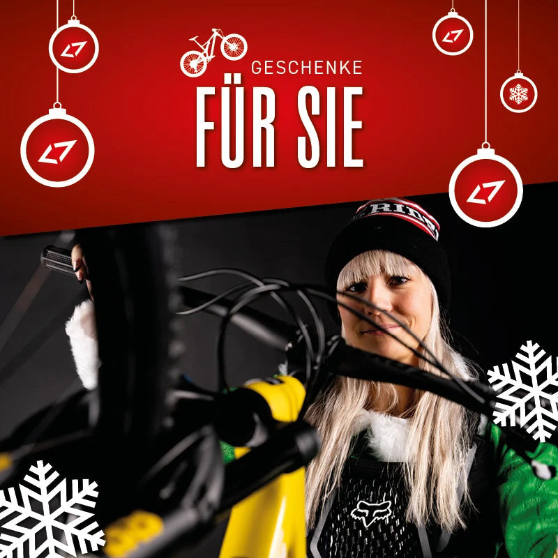 Frau mit Fahrrad und Weihnachtsdekoration, Text "Geschenke für Sie" im roten Hintergrund, Marke L7 sichtbar.