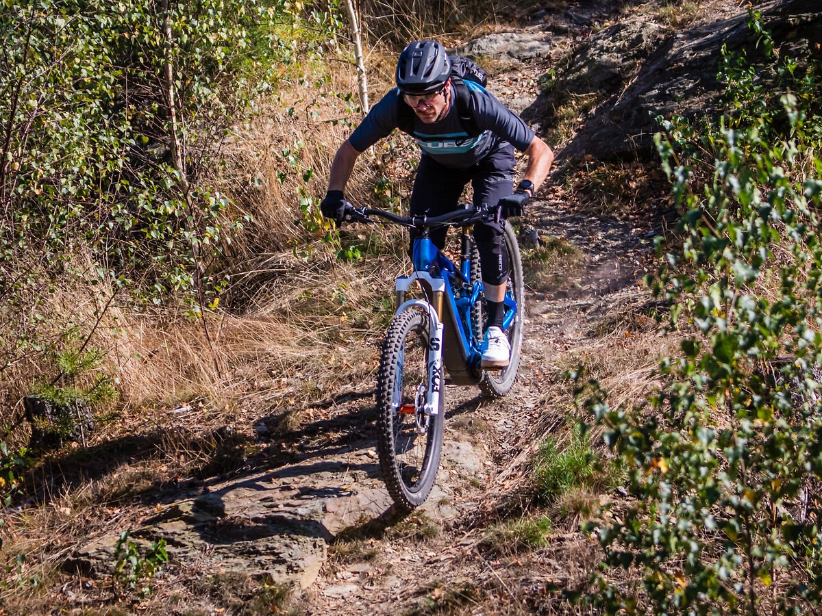 Person auf Mountainbike Cube fährt über felsigen Pfad im Wald, trägt Helm und Schutzkleidung. Modelleigenschaften nicht erkennbar.
