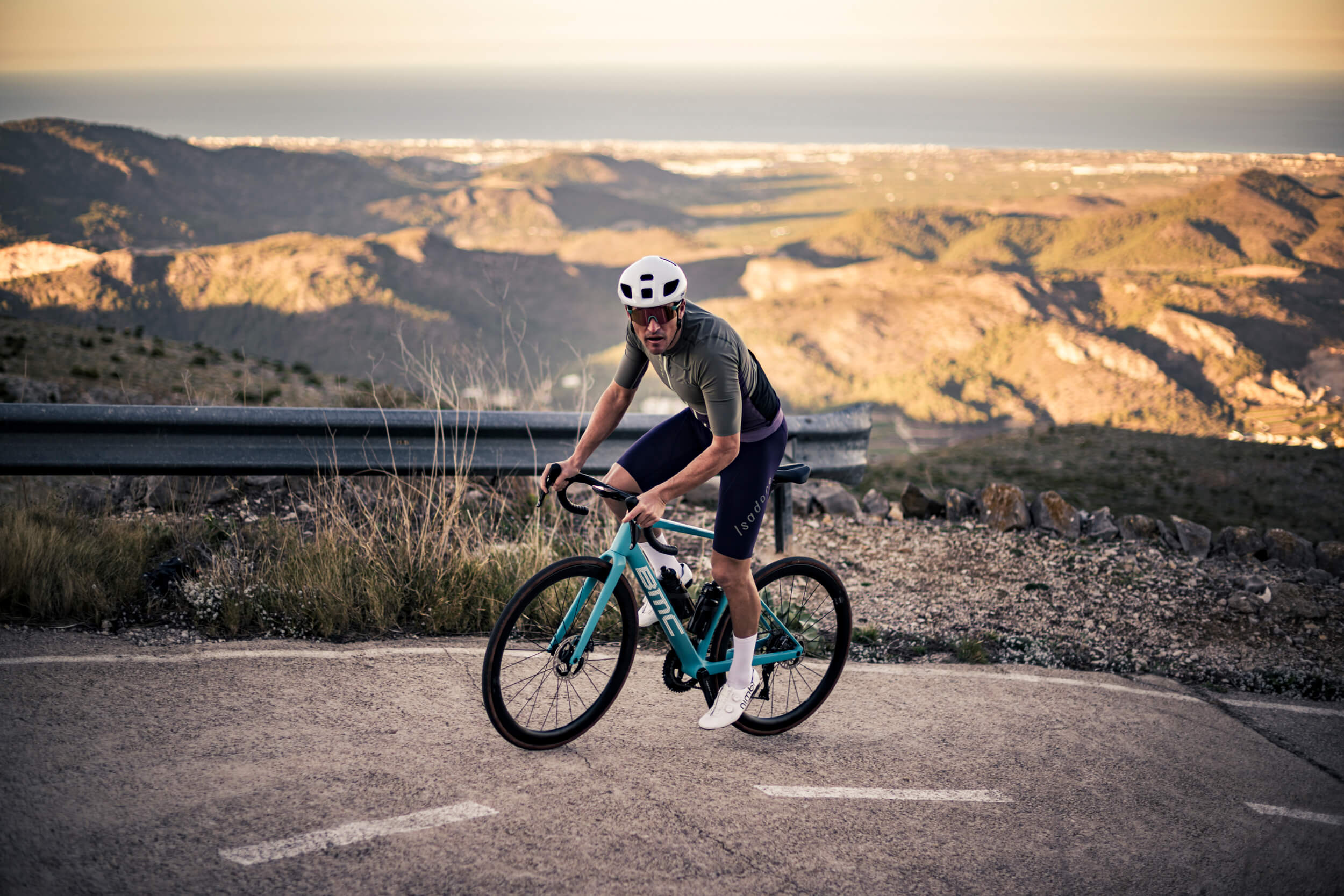 Radfahrer auf BMC Roadmachine Fahrrad in den Bergen, trägt Helm und sportliche Radbekleidung, Panorama im Hintergrund.