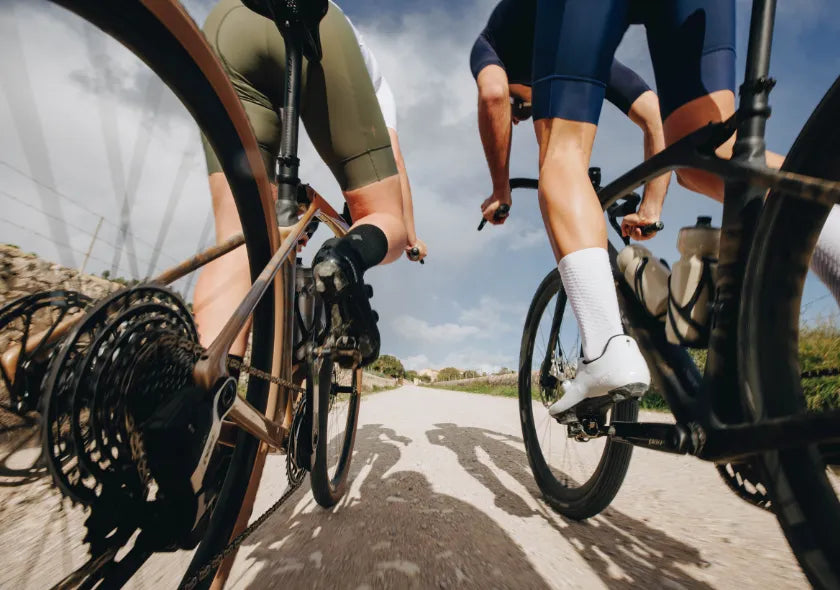 Radfahrer auf Schotterstraße, Fokus auf Hinterräder und Ketten, sportliche Bekleidung, Outdoor-Fahrradtour.
