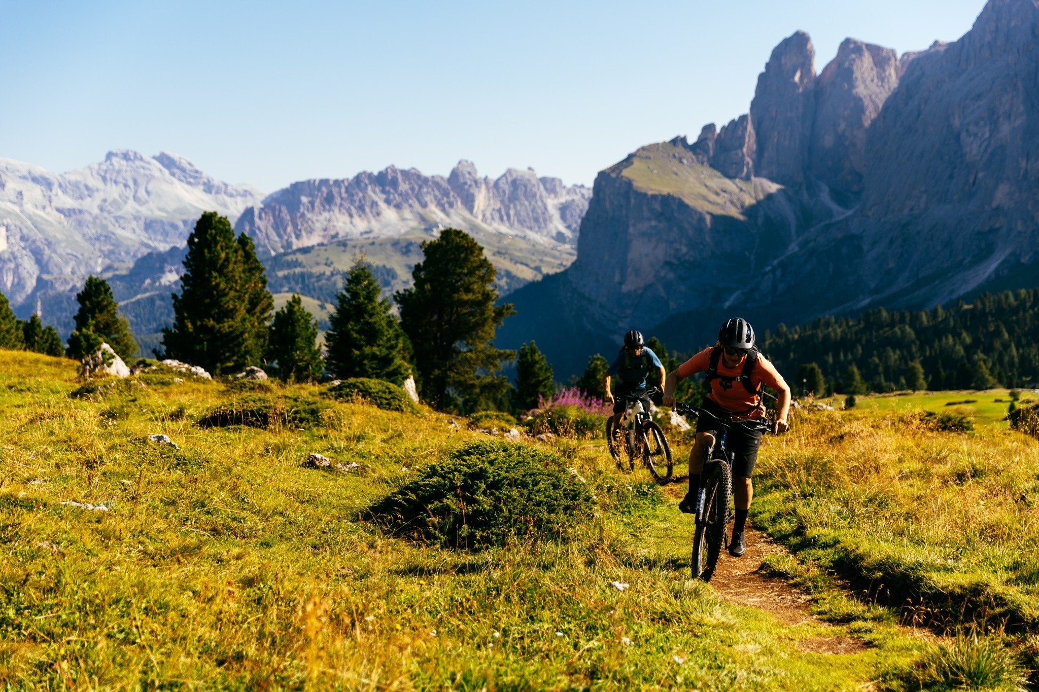 Zwei Fahrradfahrer auf Trek Powerfly E-Mountainbikes auf einem Bergpfad in alpiner Landschaft bei Sonnenschein.