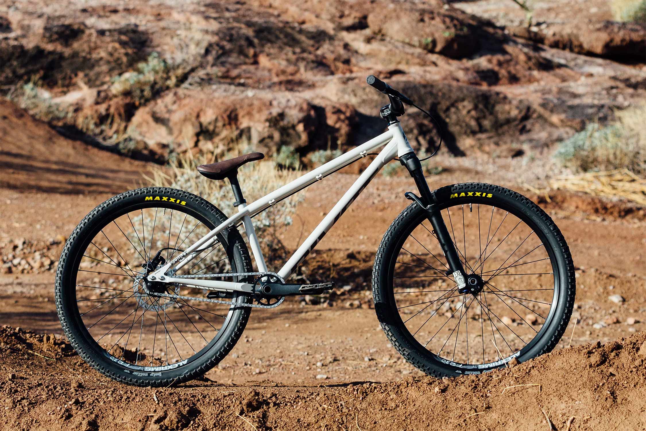Weißes Pivot Dirtbike mit Maxxis-Reifen auf einer erdigen Geländepiste.