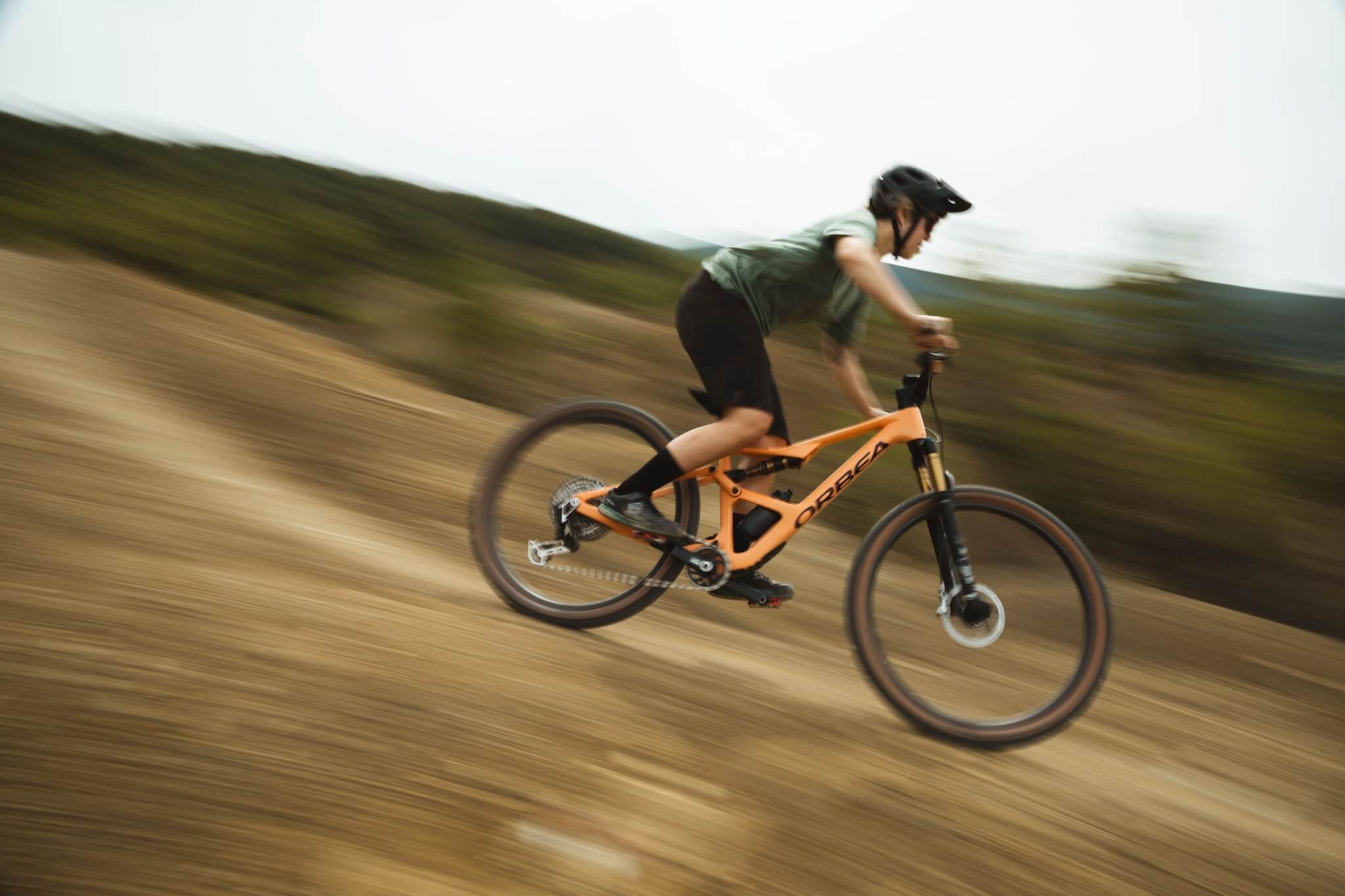 Person fährt mit einem orangefarbenen Orbea Mountainbike schnell eine sandige Piste hinunter.