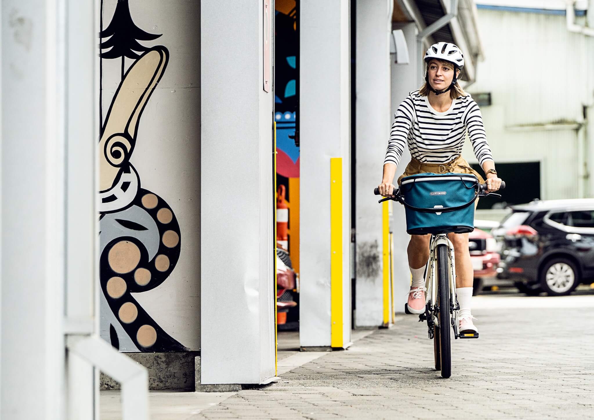 Person auf einem Fahrrad mit einer Ortlieb Fahrradtasche, trägt einen Helm, urbanes Umfeld, ideal für City-Touren.